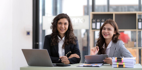 Two young Asian business woman talk, consult, discuss working with new startup project idea presentation analyze plan marketing and investment in the office.