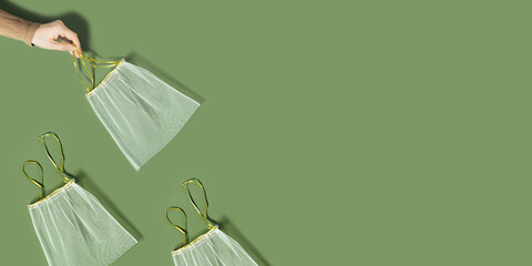 Hand holding reusable produce bags, diy from textile, reusable packaging for fruits and vegetables, mesh bag with ties, eco friendly and zero waste concept, flatlay on olive color background