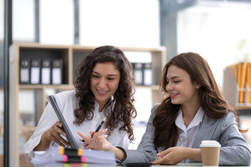 Two young Asian business woman talk, consult, discuss working with new startup project idea presentation analyze plan marketing and investment in the office.