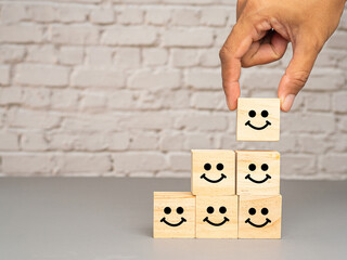 Satisfaction concept. Wooden cubes with stacked smile icons over a table with white brick wall background