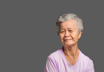 An elderly Asian woman looking at the camera with a smile while standing on a grey background