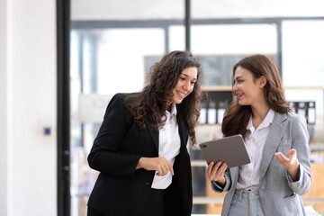 Obraz premium Two beautiful Asian businesswomen standing using digital tablet consulting and analyzing information in office work.