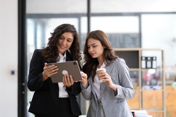Obraz premium Two beautiful Asian businesswomen standing using digital tablet consulting and analyzing information in office work.
