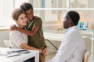 Mom with son smiling while talking to doctor about treatment during their visit at clinic