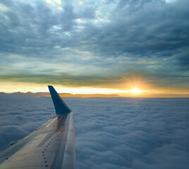Fototapeta premium view from airplane window flying over dense clouds at the sunrise