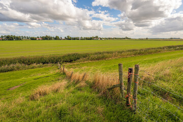 Simple fence on the slope of a grassy dike in an agricultural polder landscape. The photo was taken on a cloudy day at the end of the summer season in the Dutch province of South Holland.