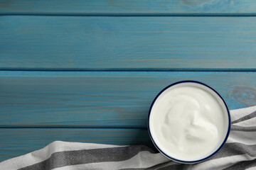 Bowl of tasty yogurt on light blue wooden table, top view. Space for text