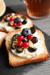 Tasty sandwiches with cream cheese, blueberries, red currants and lemon zest on slate plate, closeup
