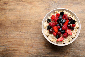 Bowl with tasty oatmeal porridge and berries on wooden table, top view. Space for text