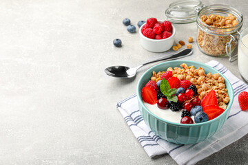 Bowl with tasty granola and berries on light grey table. Space for text