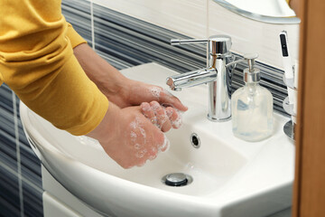 Man washing hands with soap over sink in bathroom, closeup