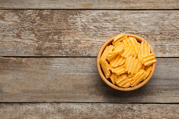 Bowl with delicious ridged potato chips on wooden table, top view. Space for text