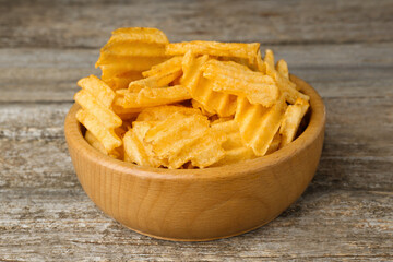 Bowl with delicious ridged potato chips on wooden table, closeup