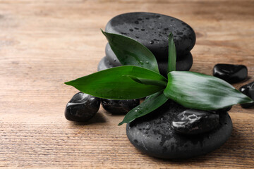 Wet spa stones and bamboo leaves on wooden table, closeup