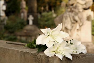 White lilies on grey tombstone outdoors, space for text . Funeral ceremony © New Africa