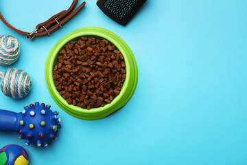 Pet toys, bowl of food and accessories on light blue background, flat lay. Space for text