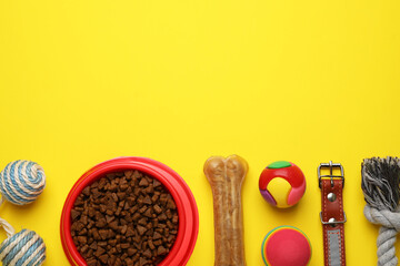 Flat lay composition with pet toys and feeding bowl on yellow background, space for text
