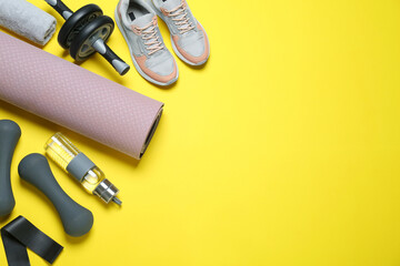 Fototapeta na wymiar Exercise mat, dumbbells, bottle of water, ab roller, fitness elastic band, towel and shoes on yellow background, flat lay. Space for text