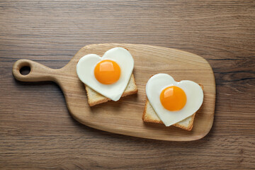 Heart shaped fried eggs and toasts on wooden table, top view