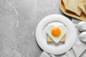 Heart shaped fried egg served on grey marble table, space for text