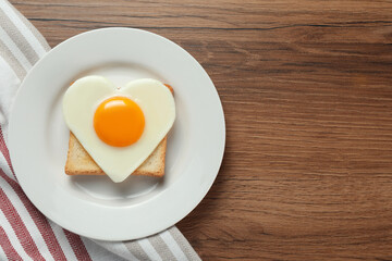 Plate with heart shaped fried egg and toast on wooden table, top view. Space for text
