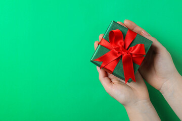 Woman holding beautifully wrapped Christmas gift box on green background, top view. Space for text