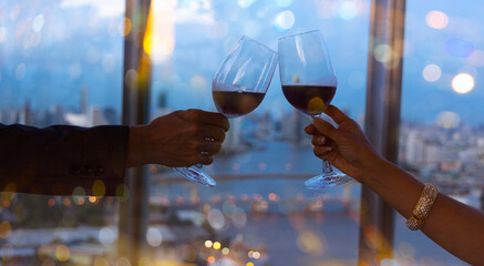 Happy lifestyle with the Couple  hand with red wine glasses which a romantic dinner on the rooftop as the sunset in a cityscape background