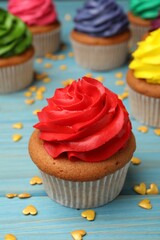 Delicious cupcake with red cream and heart shaped sprinkles on light blue wooden table