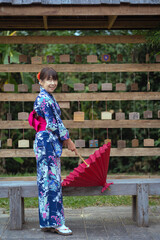 Japanese women with beautiful dresses casual Yukata Kimono and red umbrellas wear traditional clothes and stand with hold a red umbrella and wall for hanging wooden signs wishing sacred things.