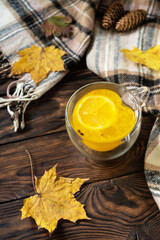 Obraz na płótnie Canvas Seasonal autumn concept with drink. Cup of hot sea ​​​​buckthorn tea with lemon, warm scarf and maple leaves on rustic background.