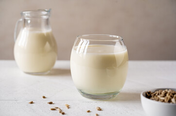 Sunflower milk in glass with raw seeds, milk jar on white wooden background