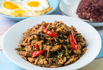 Spicy fried pork with basil leaves, the famous traditional Thai food served with riceberry and fried egg.