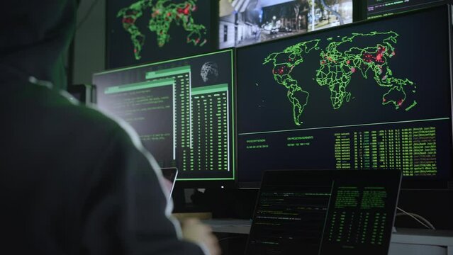 Criminal Hacker using computer pointing to a world map for organizing global massive data breach attack on government and big company servers. Dark room surrounded computers. High quality 4k footage