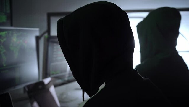 Back hooded hacker using malicious software hack corporate data center. malefactor hidden underground in dark place, multiple displays with phishing code and global map attack. High quality 4k footage