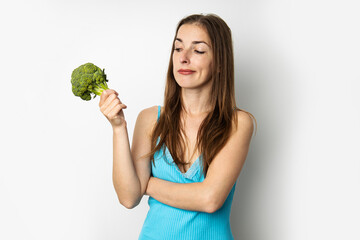 Thoughtful young woman holding green fresh broccoli on white background