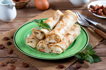 Rolled pancakes with cottage cheese and raisins on rustic wooden table
