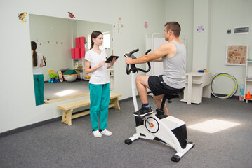 Young man exercising during physiotherapy with physiotherapist in modern medical rehabilitation...