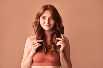 Attractive young woman in lingerie with red hair touching her hair on a beige background. Woman...