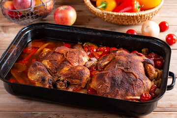 Whole baked golden crispy chicken in a baking dish cooked with vegetables on wooden table