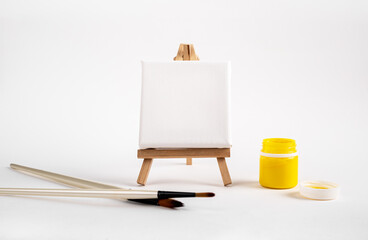 Square canvas mockup on wood tripod with drawing brushes and yellow paint jar