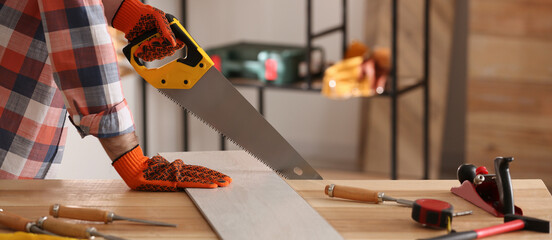 Carpenter sawing wooden plank at table in workshop, closeup. Banner design