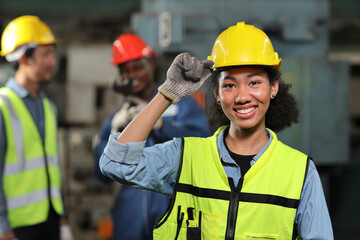 Confident technician engineer woman in protective suit standing and touching her hardhat while looking camera and maintenance operation work lathe metal machine at heavy industry manufacturing factory