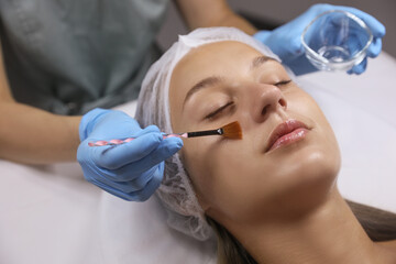 Fototapeta premium Cosmetologist applying chemical peel product on client's face in salon