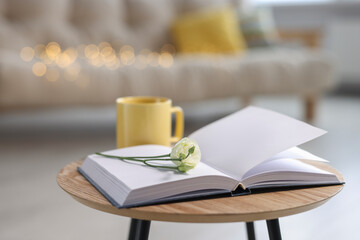 Naklejka na ściany i meble Yellow mug, open book and eustoma flower on wooden table in living room