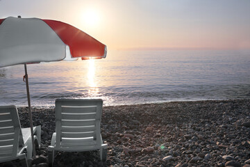 Empty sunbeds and umbrella on stone beach at sunset