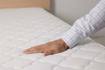 Man touching soft white mattress indoors, closeup