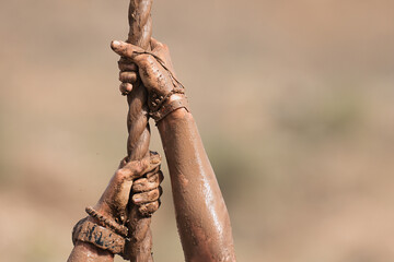 Mud race runner. Detail of muddy hands they climb the rope. Athletic man working out and climbing a rope, during obstacle course