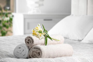 Fototapeta na wymiar Terry towels with beautiful flowers on bed indoors, space for text