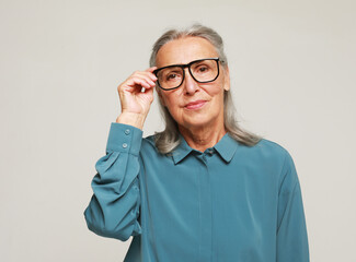 Elderly woman looking through her eyeglasses isolated on grey background