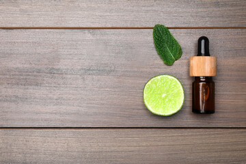 Bottle of citrus essential oil and fresh lime on wooden table, flat lay. Space for text
